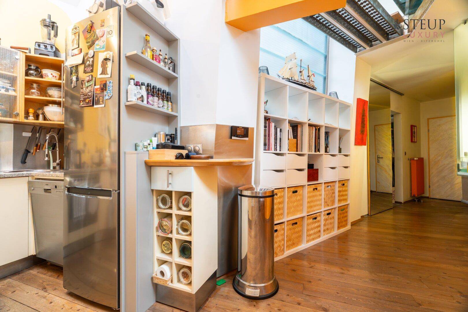Küchenbereich mit großem Kühlschrank, praktischen Regalen und Holzboden.