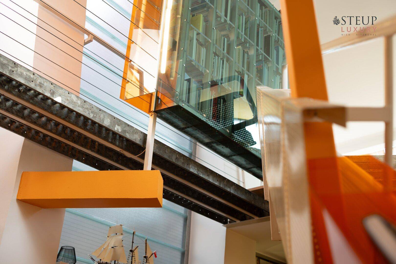 Architektonisches Detail des Treppenbereichs mit Metallträgern und einem Bücherregal aus Glas.