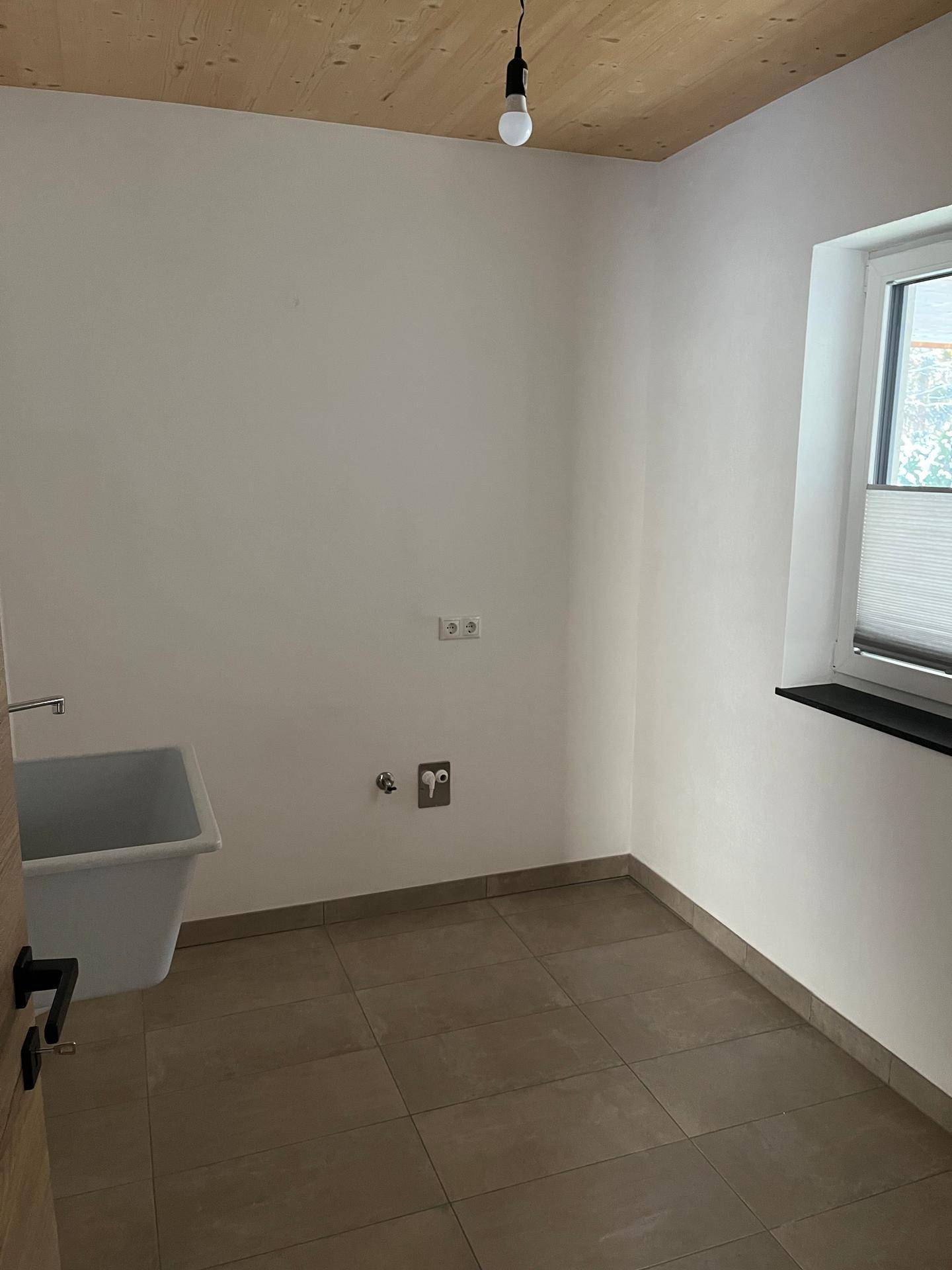 Praktischer Hauswirtschaftsraum mit Waschbecken, Fliesenboden und Fenster.