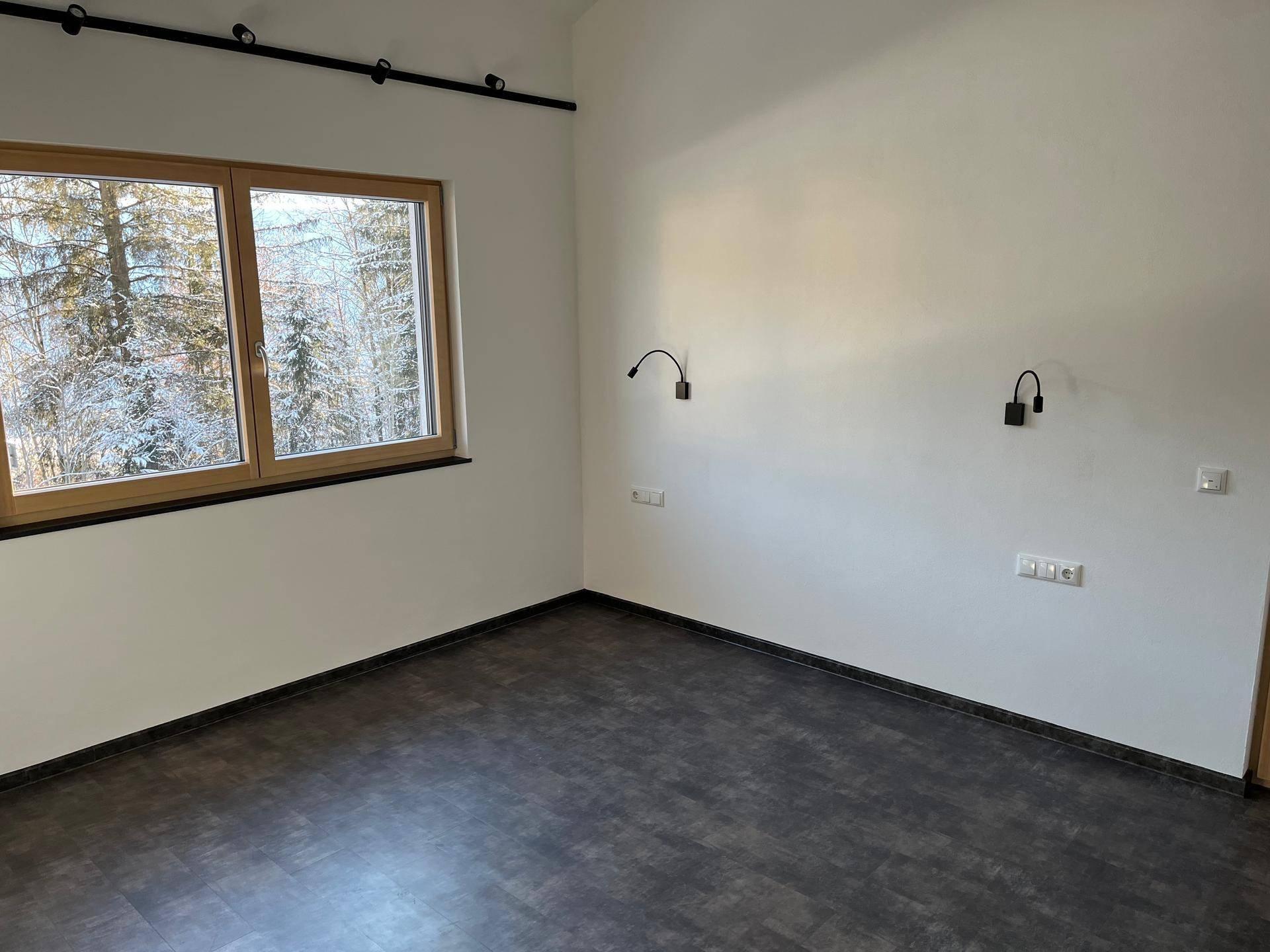 Schlafzimmer mit dunklem Boden, Holzdecke und weitem Blick auf die verschneiten Bäume.