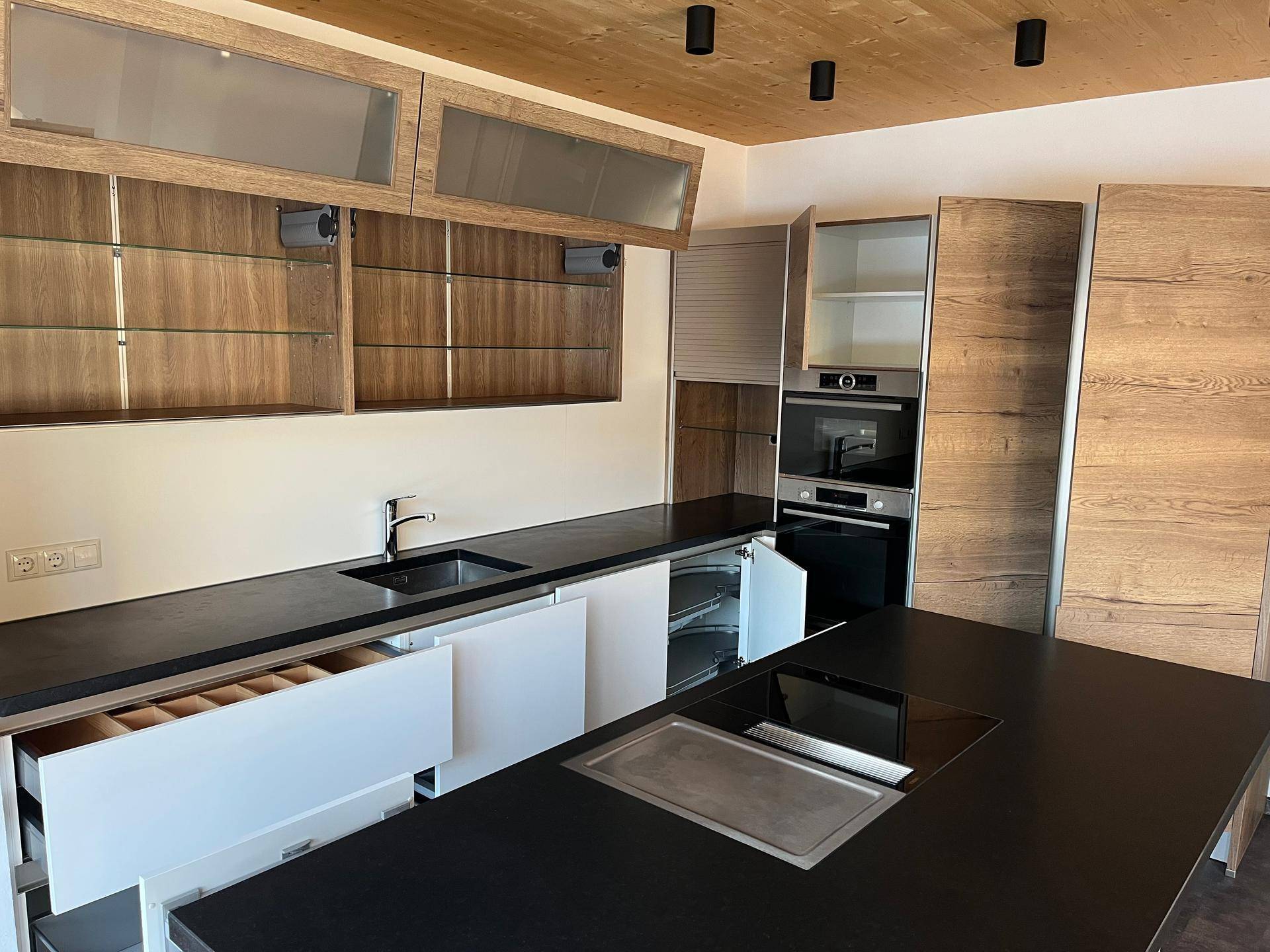 Moderne Küche mit Holzdecken, dunklen Arbeitsplatten und integrierten Geräten.