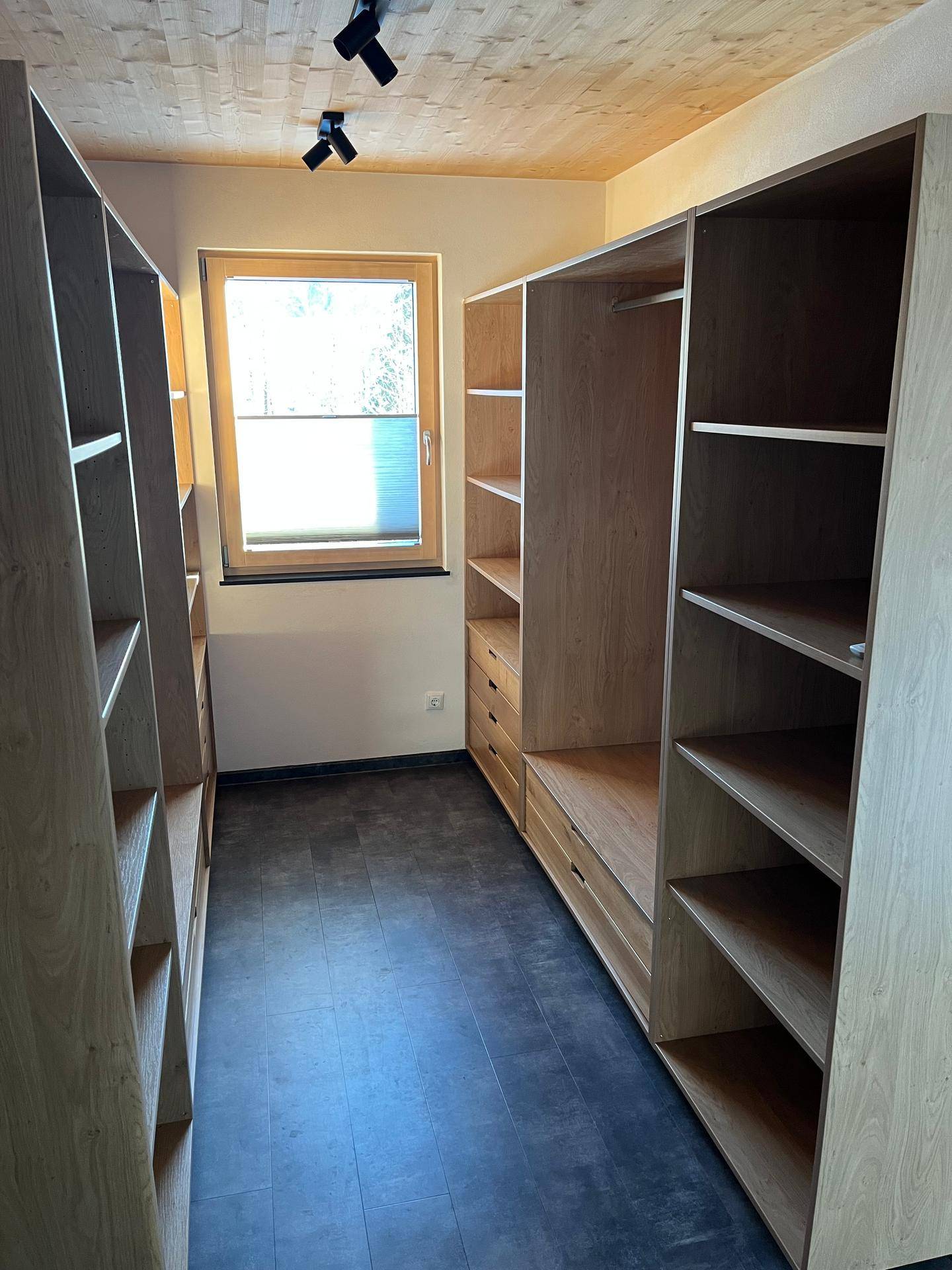 Begehbarer Kleiderschrank mit maßgefertigten Holzregalen und dunklem Boden.