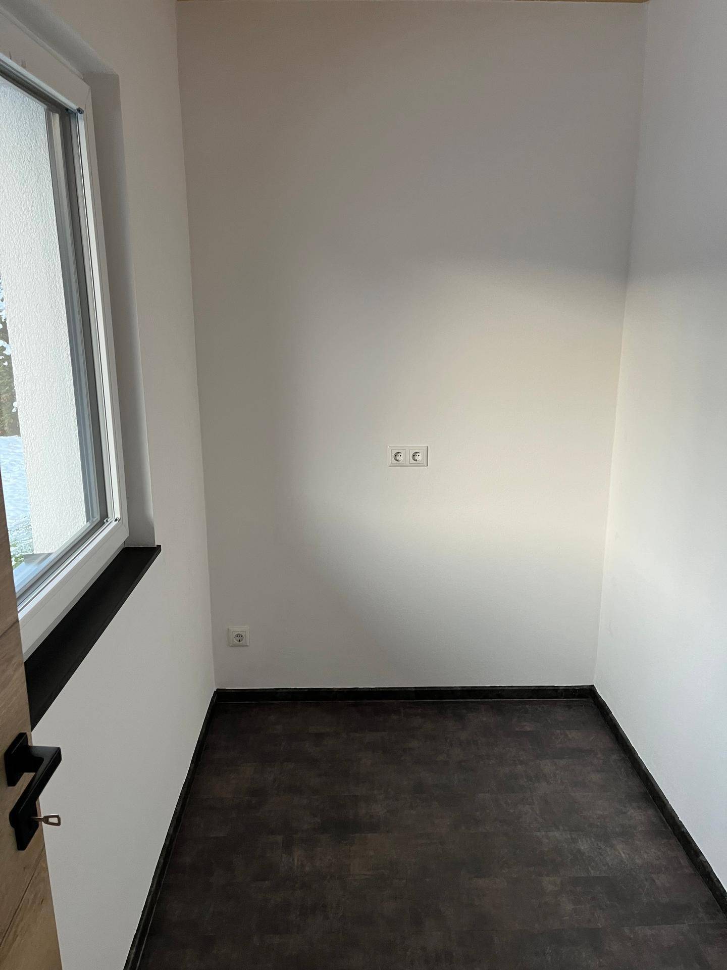 Kleiner, heller Raum mit Fenster und dunklem Boden, vielseitig nutzbar.