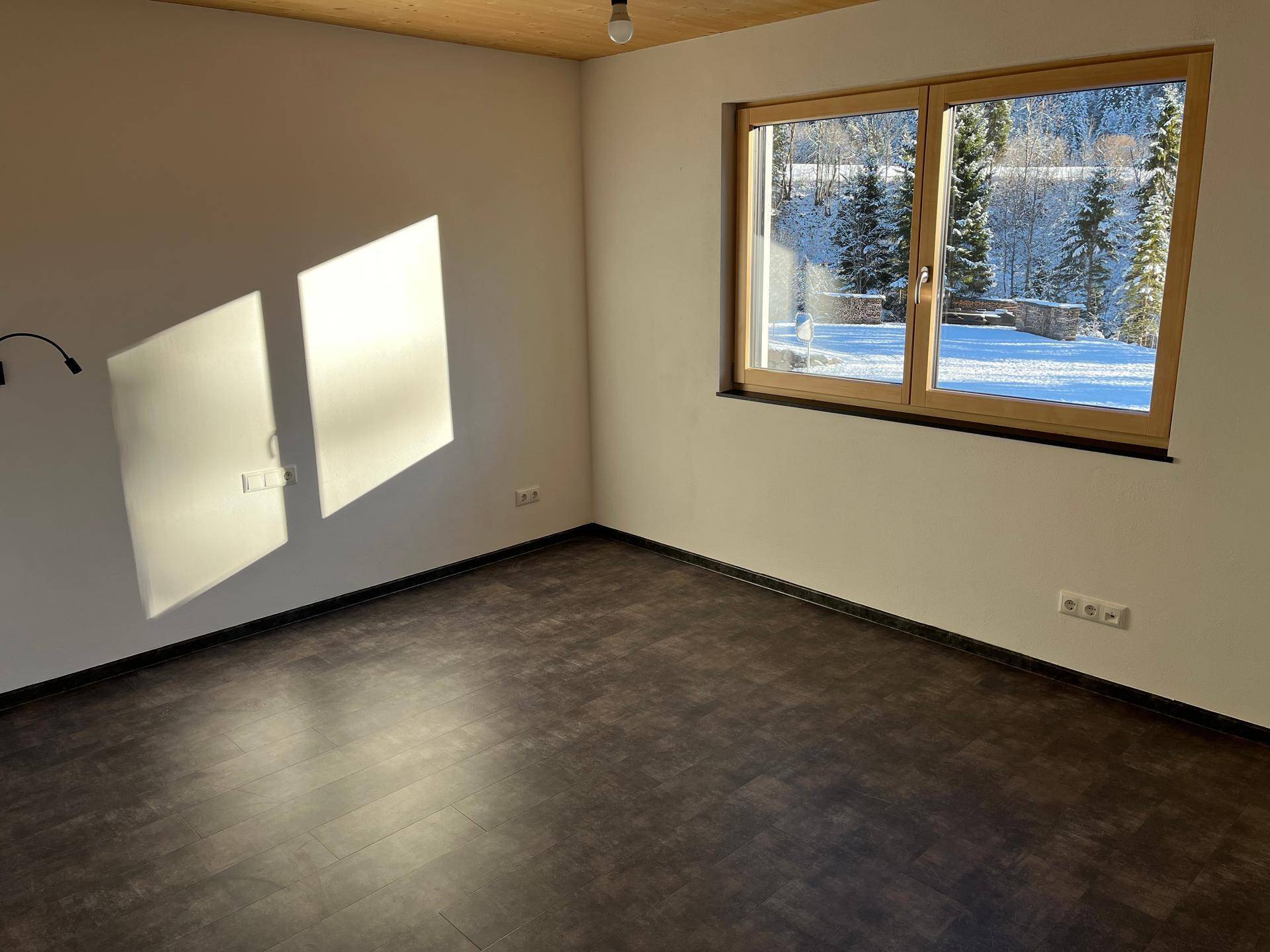 Sonniges Schlafzimmer mit dunklem Boden, Holzdecke und Blick auf die verschneite Landschaft.