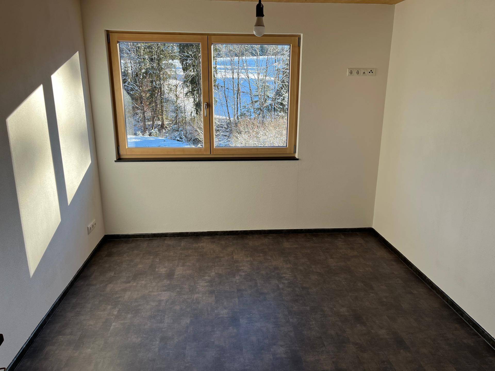 Helles Schlafzimmer mit dunklem Boden, Holzdecke und weitem Blick in die Natur.