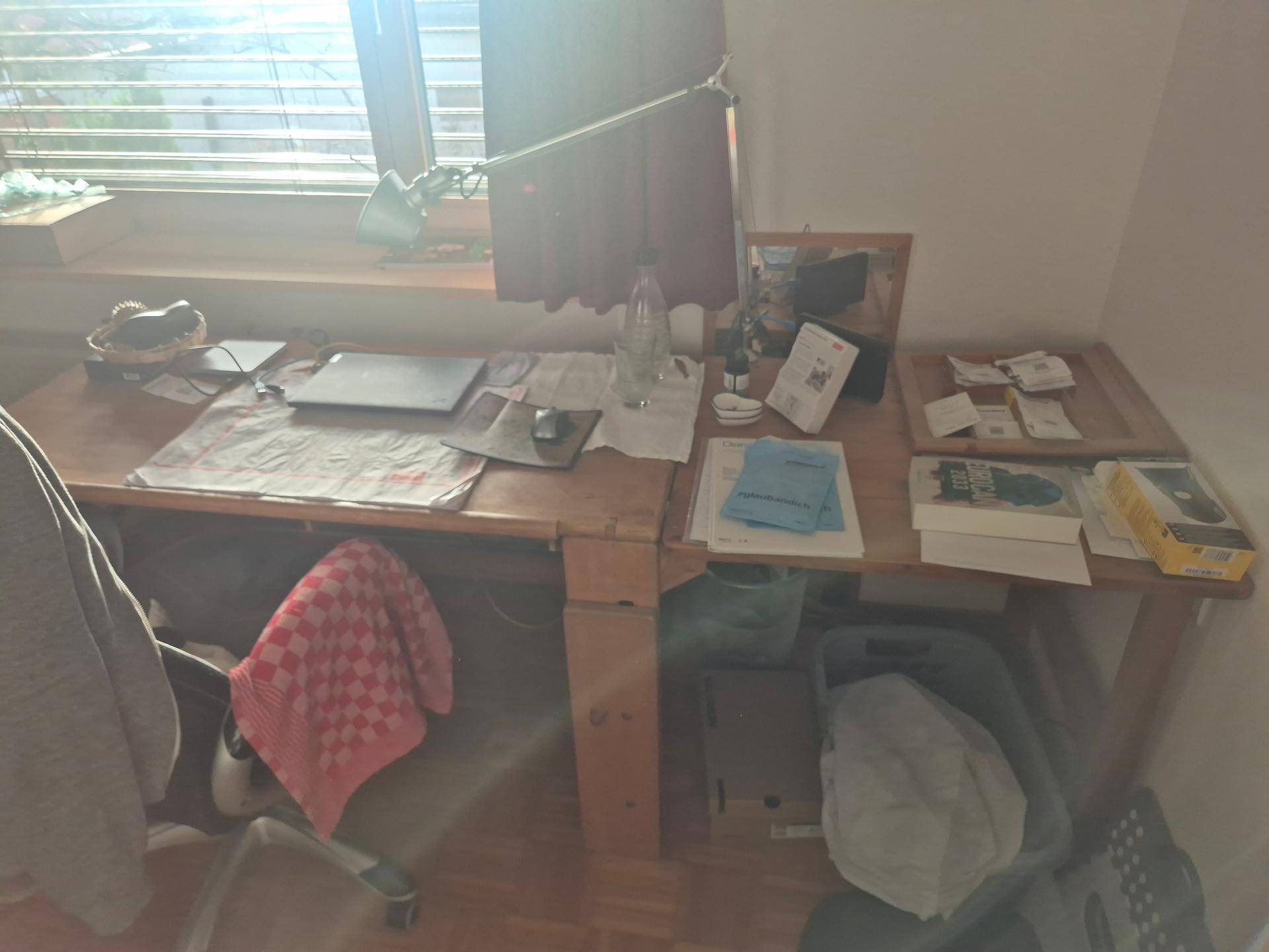 Detailansicht eines Holzschreibtisches mit Arbeitsmaterialien und natürlichem Lichteinfall.