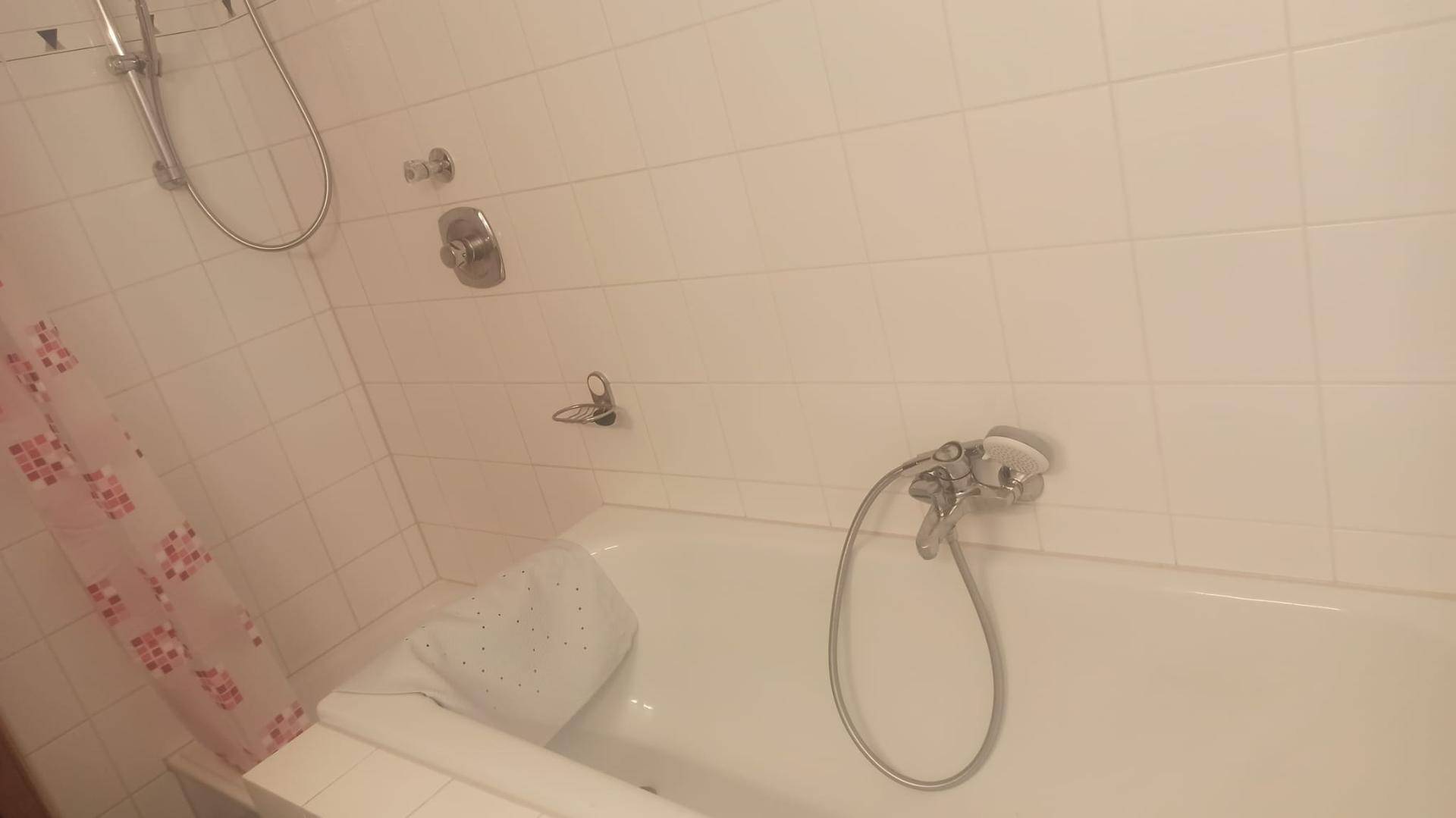 Badezimmer mit Badewanne und Duschvorrichtung, komplett gefliest.