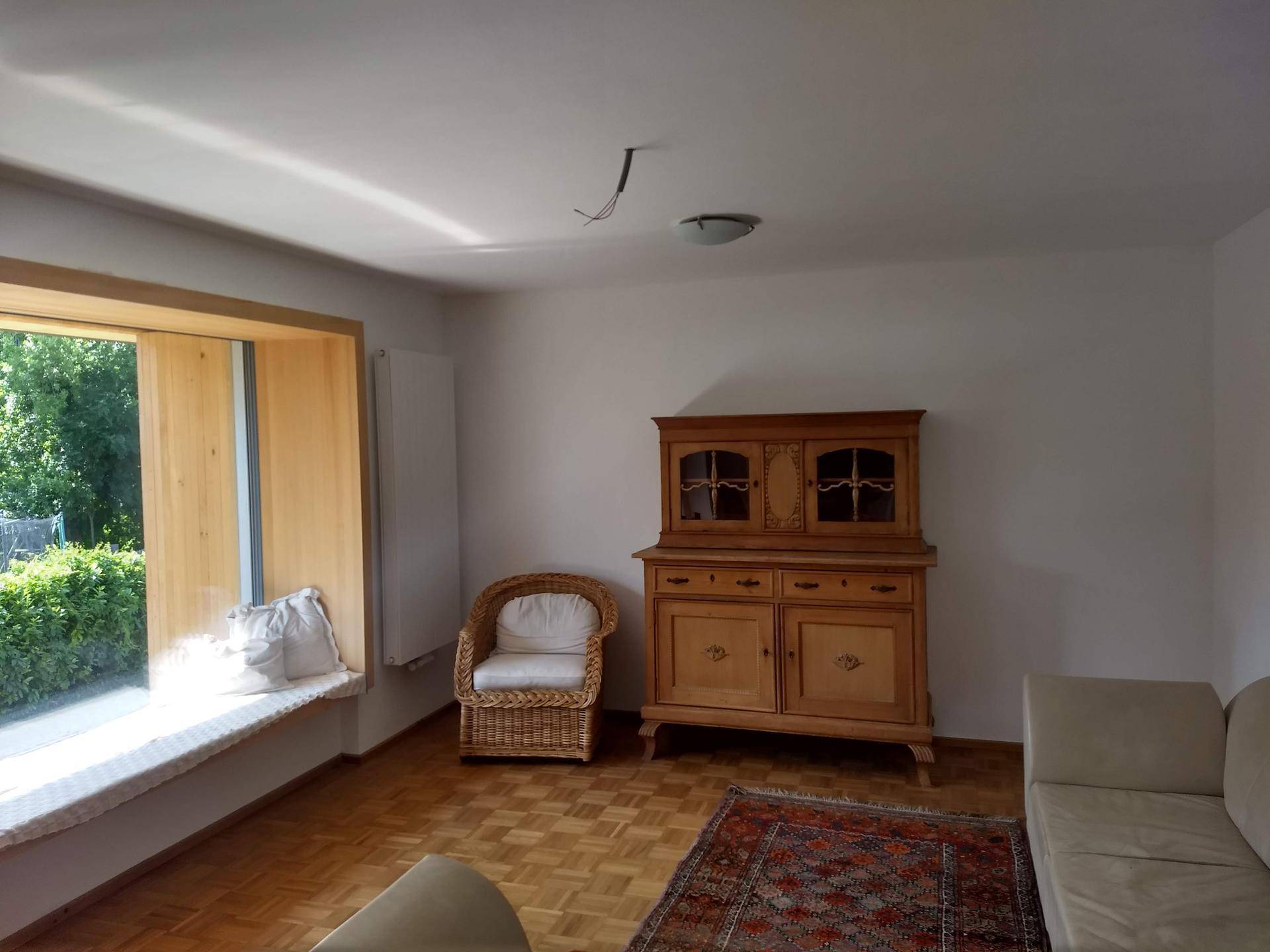 Helles Wohnzimmer mit Parkettboden, gemütlicher Fensterbank und traditionellem Holzschrank.