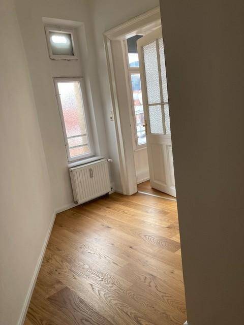 Schmaler Flur mit Eichenparkettboden, Heizkörper und Fenstern, die Tageslicht hereinlassen.