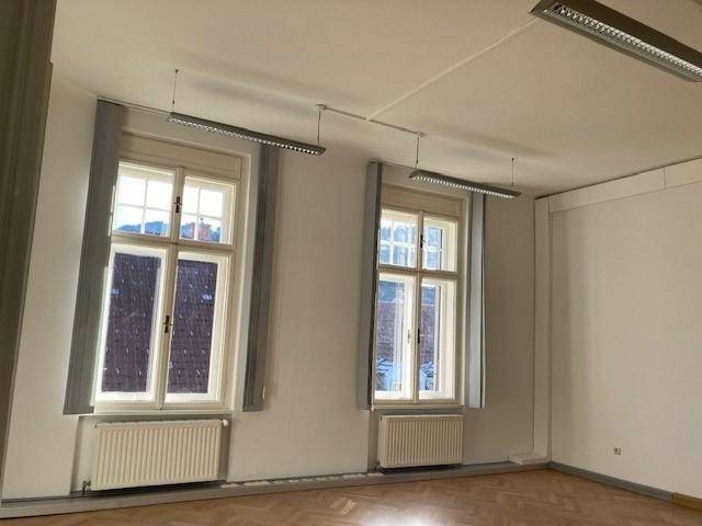 Geräumiger Raum mit zwei großen Fenstern und Parkettboden, der viel Helligkeit und eine angenehme Atmosphäre schafft.