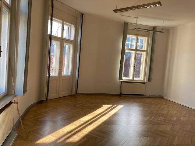 Großer, heller Raum mit zwei hohen Fenstern und Fischgrätparkett, ideal für Wohn- oder Bürozwecke.