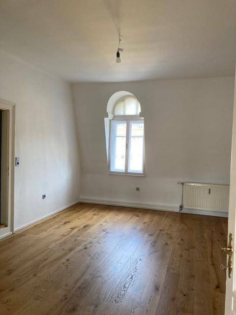 Helles Wohnzimmer mit neuem Eichenparkettboden, hohen Decken und einem eleganten Rundbogenfenster.