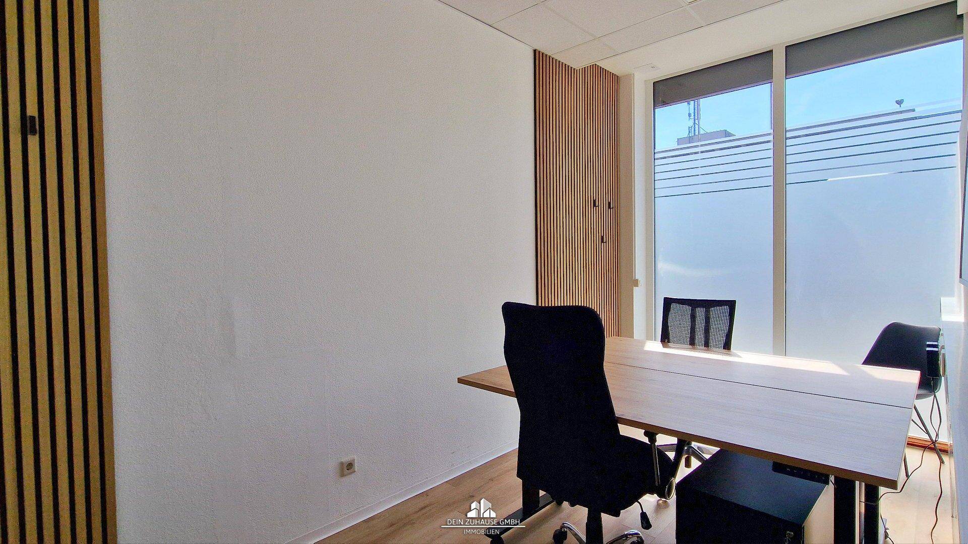 Büroraum mit Holzwandverkleidung, einem Schreibtisch und Bürostühlen, beleuchtet durch große Fenster.