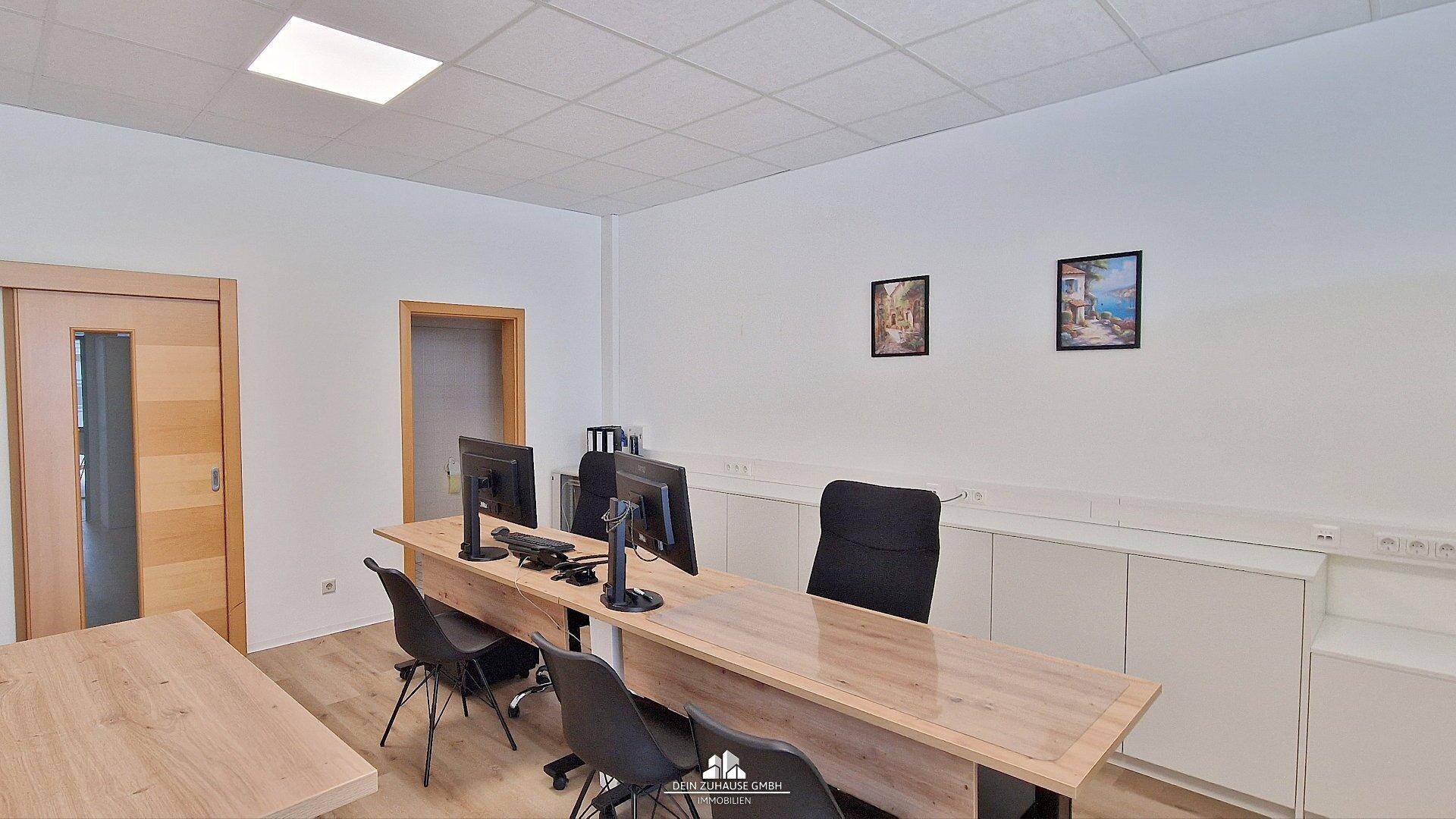 Geräumiger Büroraum mit mehreren Arbeitsplätzen, Holzschreibtischen und weißen Schränken entlang der Wand.