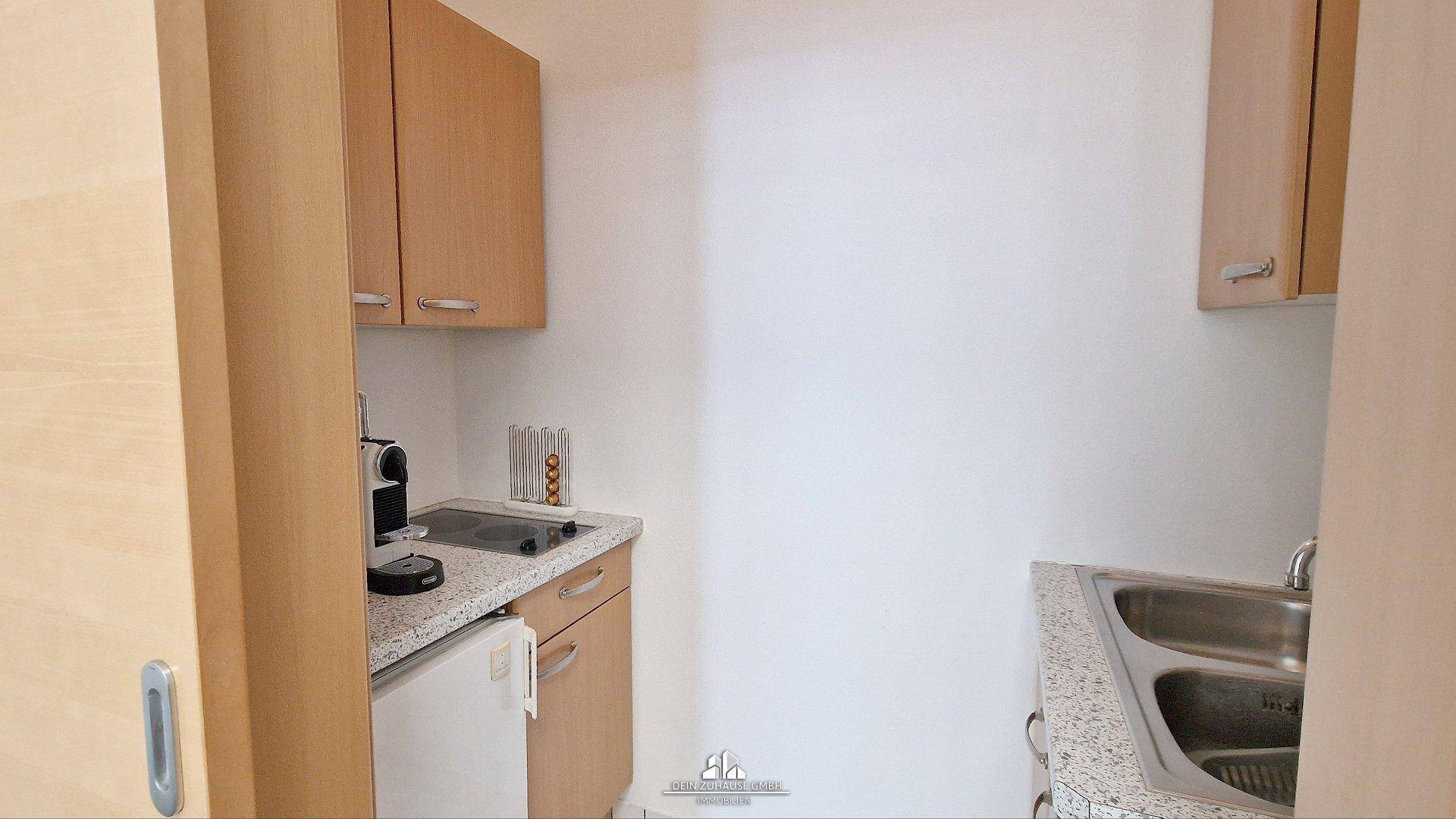 Kleine Küchenzeile mit Holzschränken, Spüle, Kochfeld und Kühlschrank, ideal für Pausen.