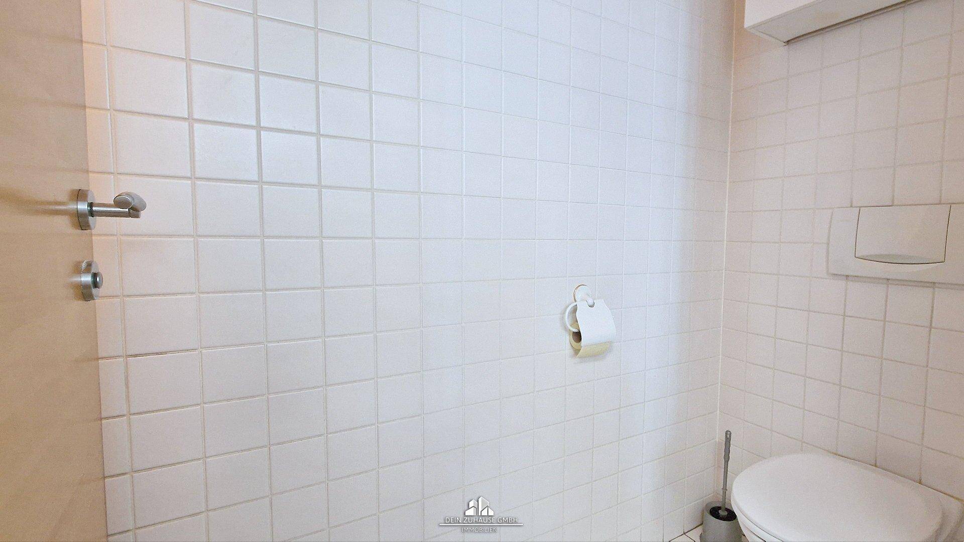 Sauberer Toilettenraum mit weißen Fliesen an den Wänden und einer wandmontierten Toilette.