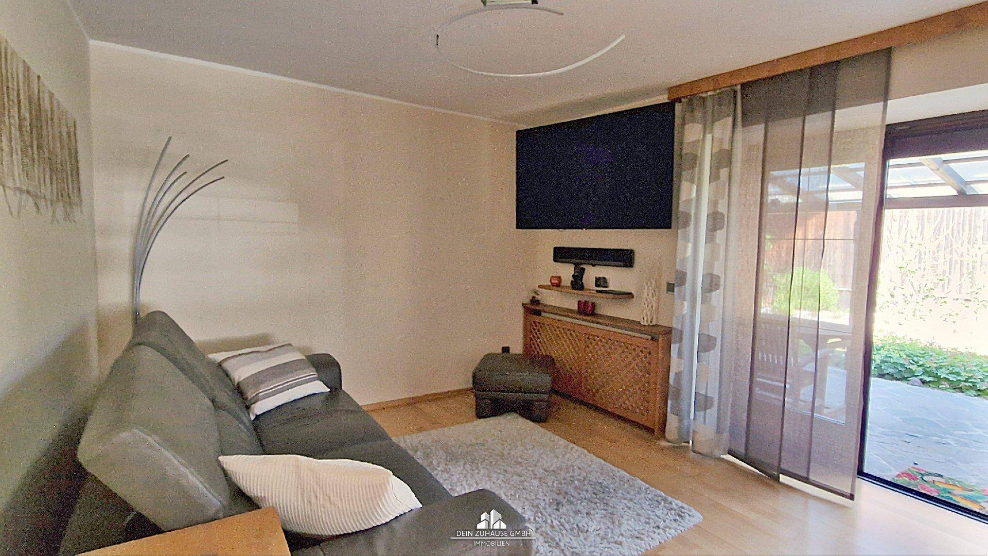 Wohnzimmer mit Sofa, Fernseher und Zugang zur überdachten Terrasse.