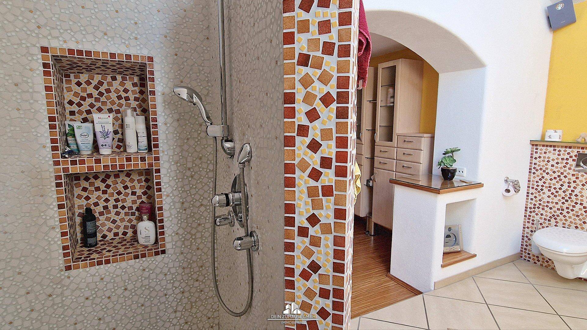 Duschbereich im Badezimmer mit Mosaikfliesen, Nischen und separatem WC.