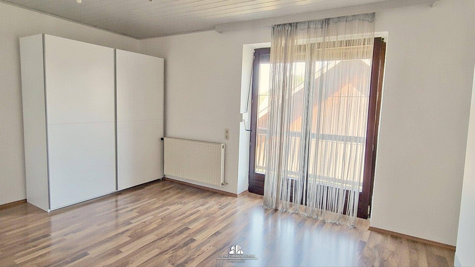 Schlafzimmer mit weißem Kleiderschrank, Holzboden und Balkonzugang.