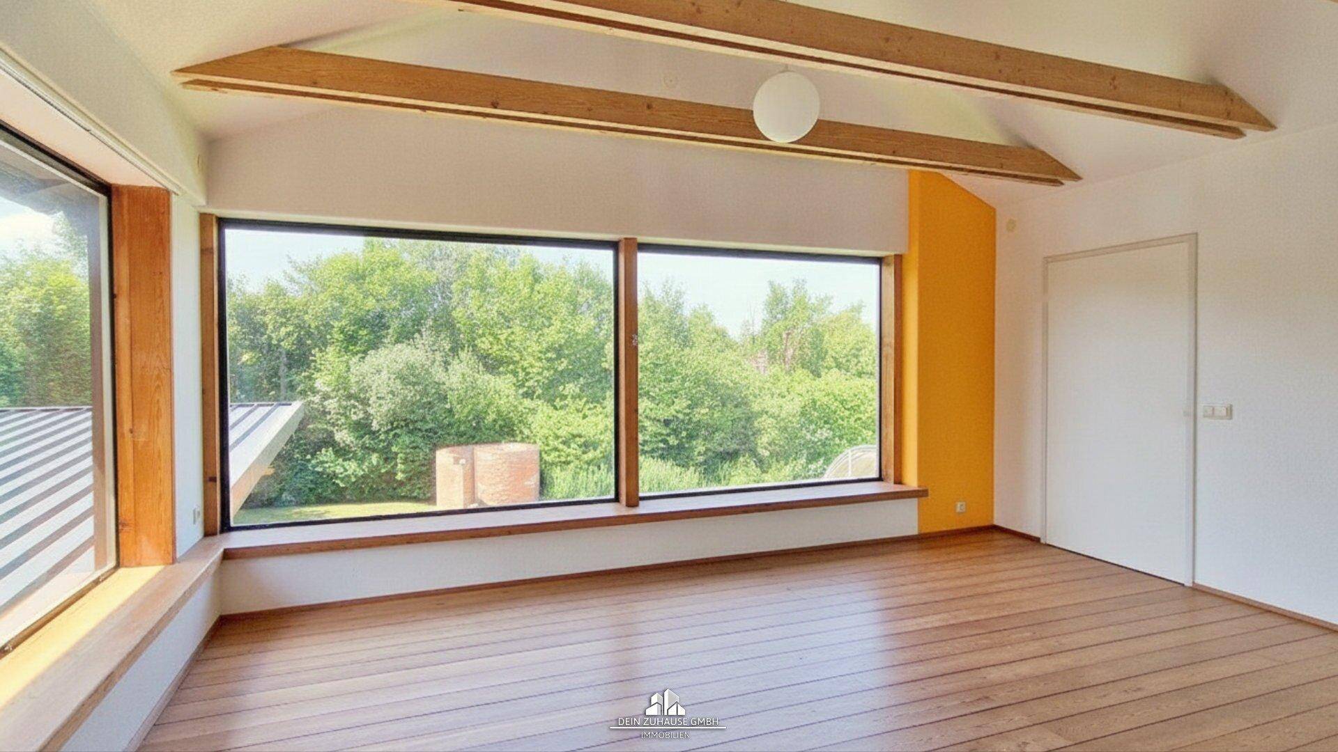 Heller Raum mit großen Panoramafenstern, Holzboden und Holzbalken an der Decke.
