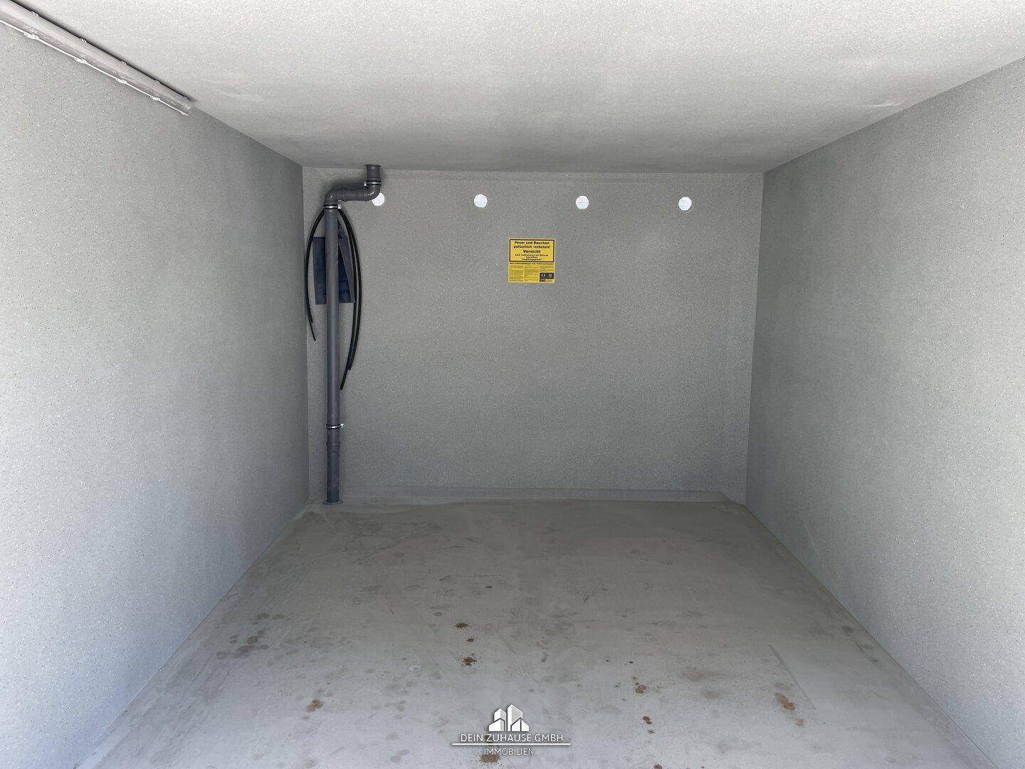 Innenansicht einer leeren Garagenbox mit sichtbaren Leitungen und Beleuchtung.