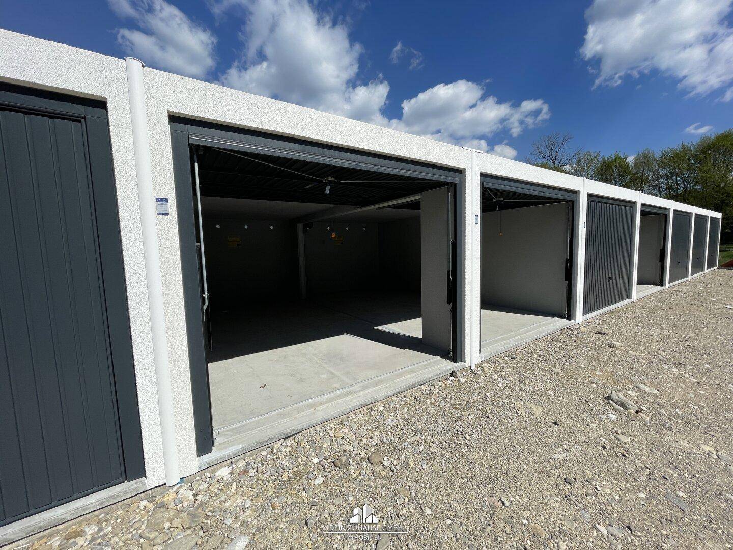 Reihe von Garagenboxen mit geöffneten Toren unter strahlend blauem Himmel.