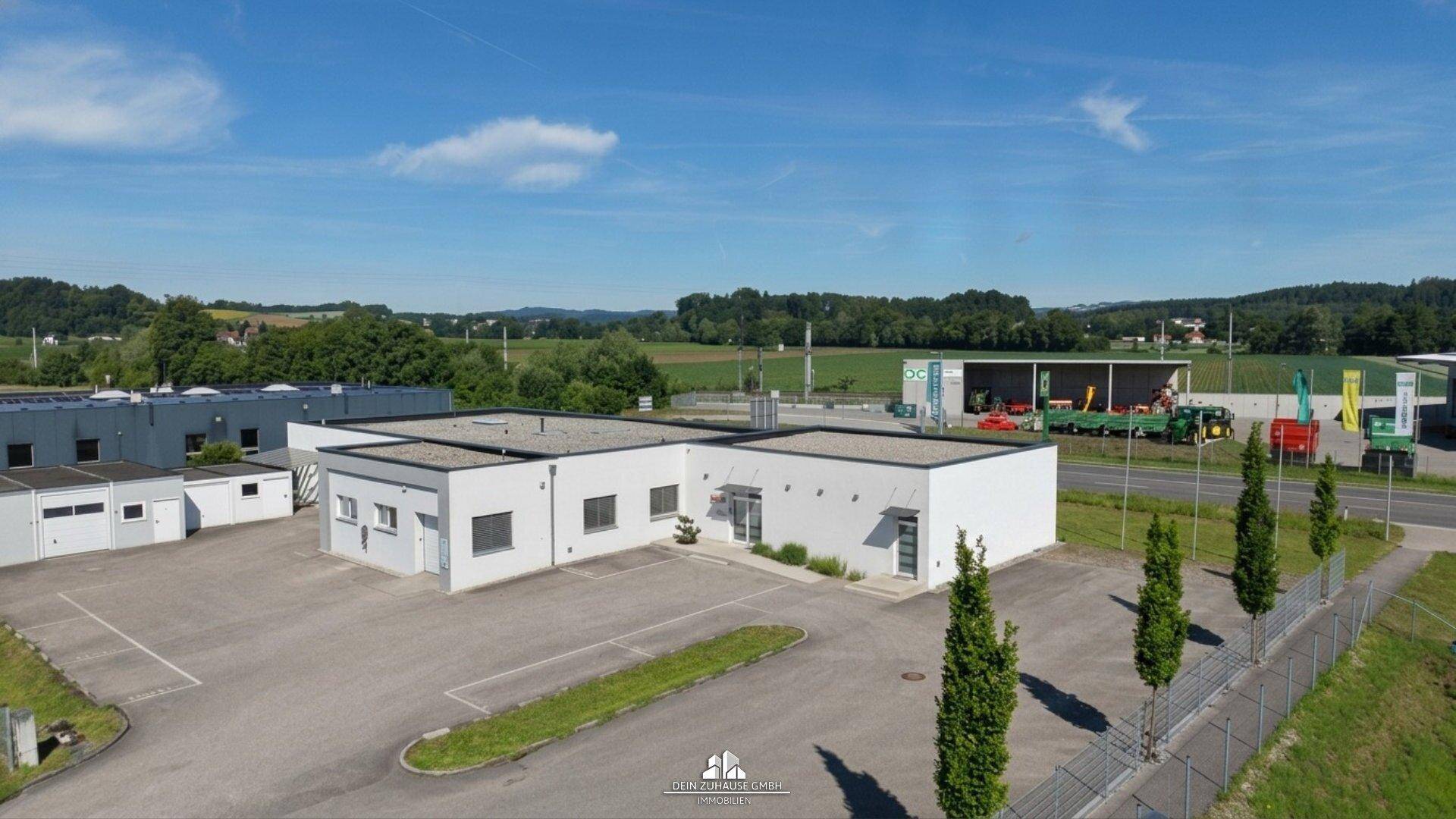 Weitläufige Luftaufnahme eines Gewerbeobjekts mit Parkplätzen und angrenzender ländlicher Umgebung.