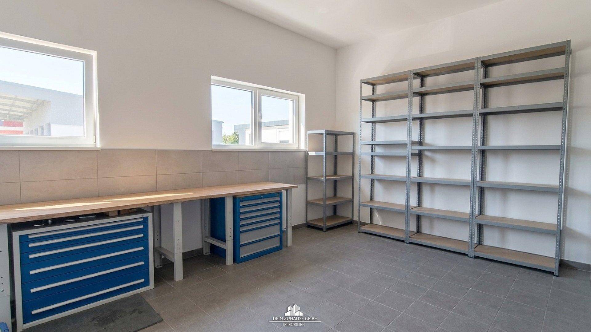 Helle Werkstatt mit Arbeitsplatte, blauen Schubladenschränken und Metallregalen.