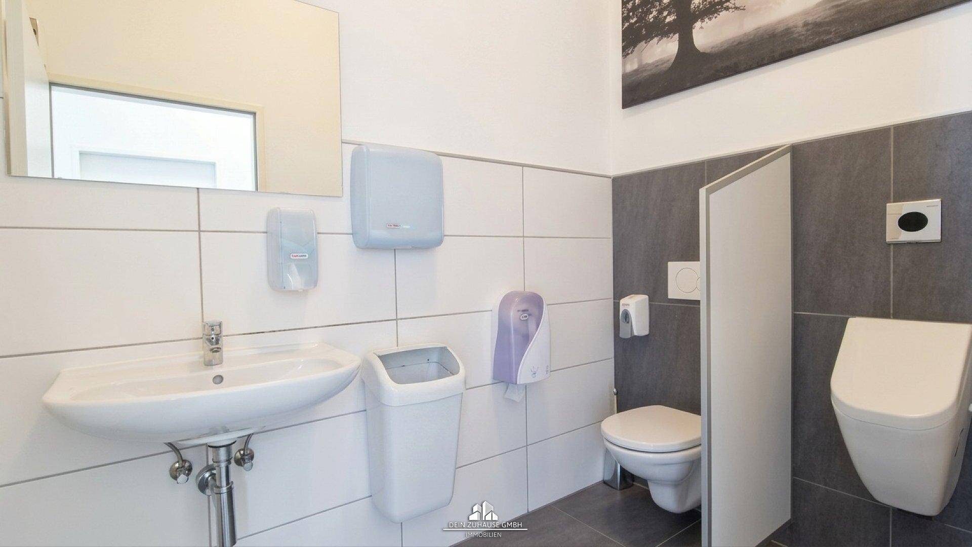 Saubere und funktionale Toilette mit Waschbecken, Spiegel und modernen Fliesen in Grau und Weiß.