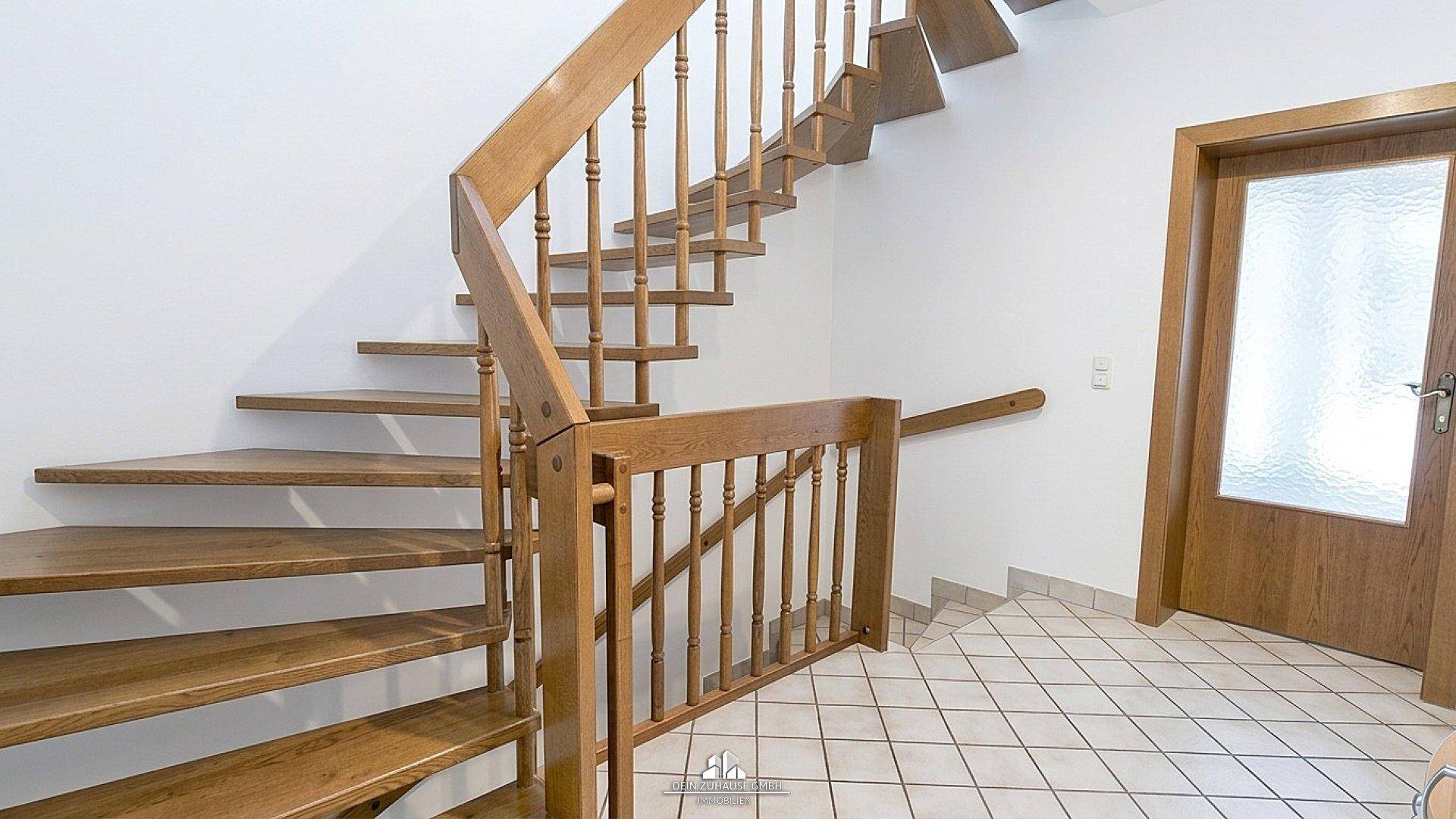 Holztreppe im Flur mit hellem Fliesenboden und weiß gestrichenen Wänden.