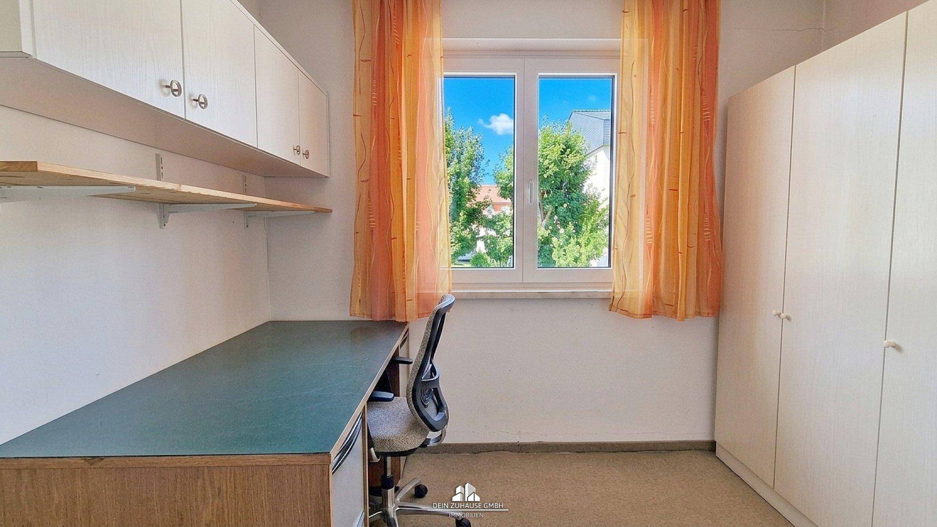 Arbeitszimmer mit Schreibtisch, Schrank und Blick ins Grüne.