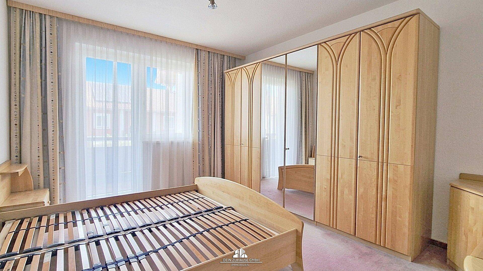 Schlafzimmer mit hellem Holzbett, großem Spiegelschrank und Fenster.