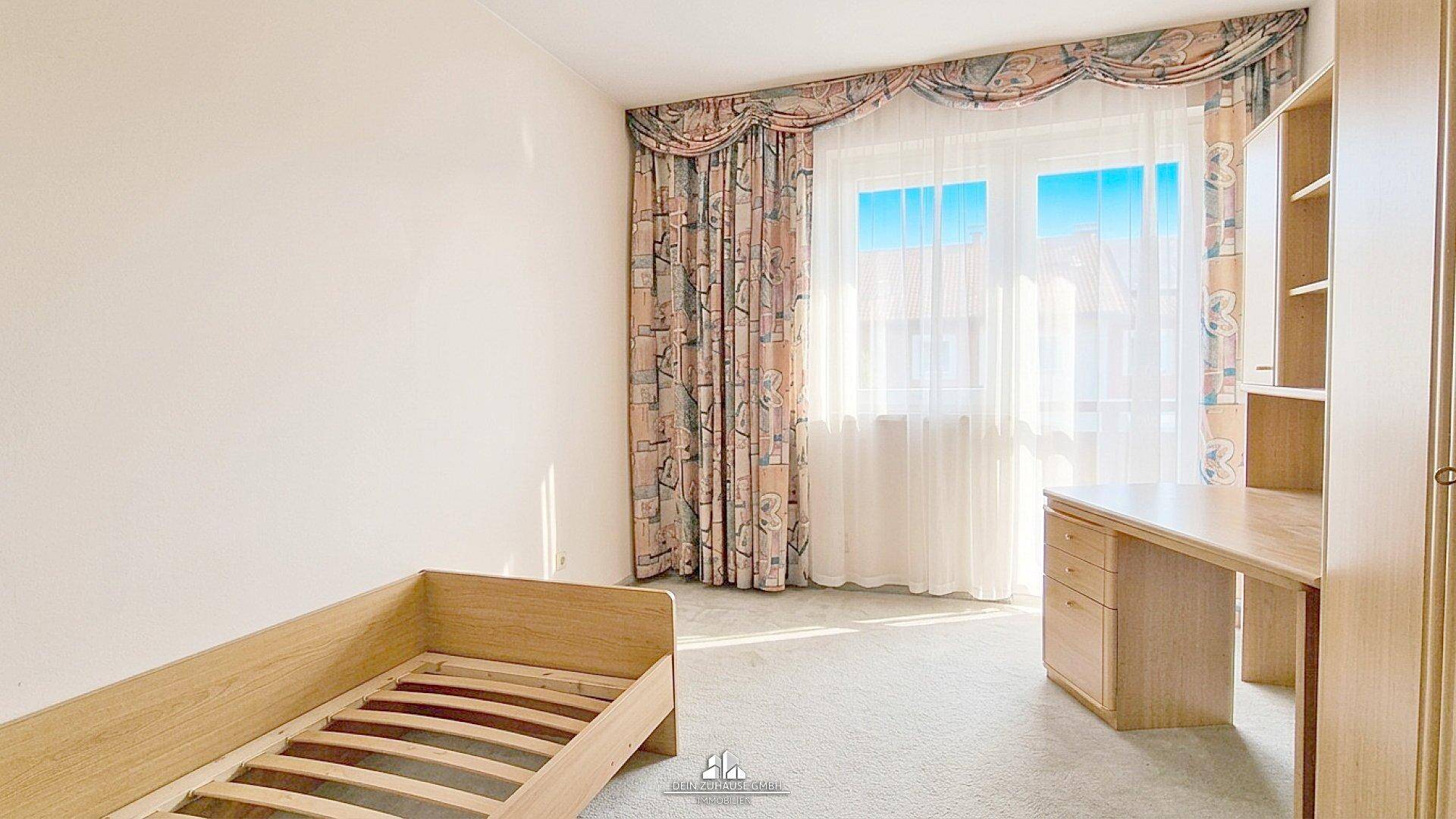 Helles Zimmer mit Teppichboden, Schreibtisch und großem Fenster.