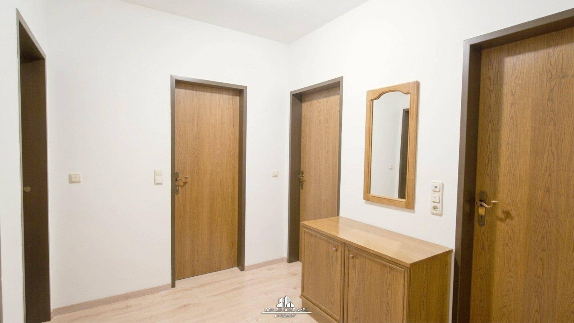 Heller Flur mit mehreren Holztüren und einem kleinen Holzschrank.