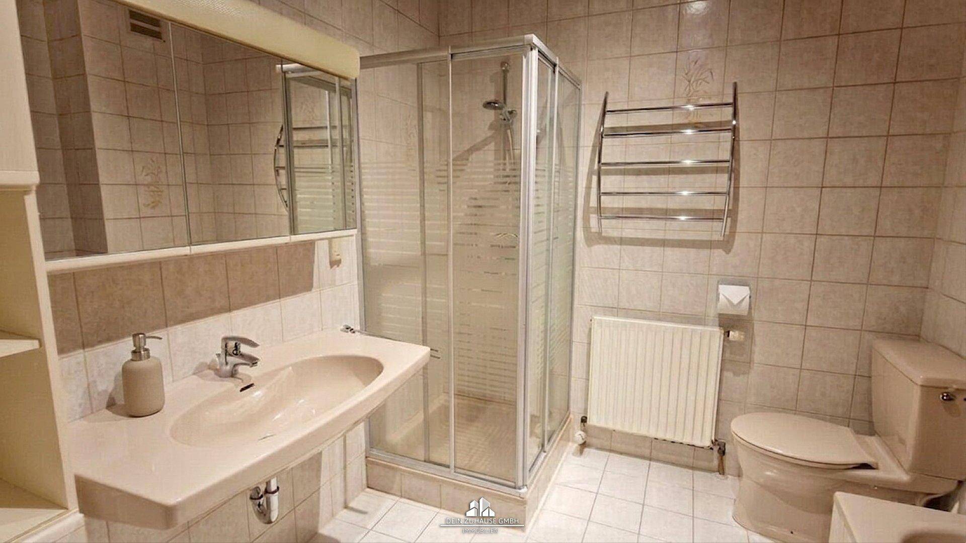 Badezimmer mit Duschkabine, Waschbecken und beheiztem Handtuchhalter.