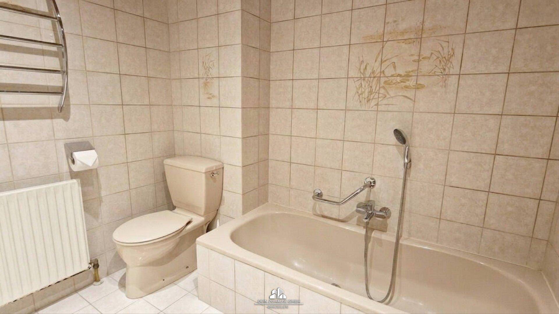 Badezimmer mit Badewanne, Toilette und hellen Fliesen.