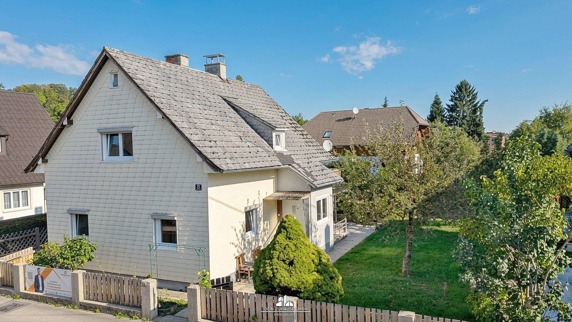 Seitenansicht des Einfamilienhauses mit Holzfassade, Satteldach und umzäuntem Vorgartenbereich.
