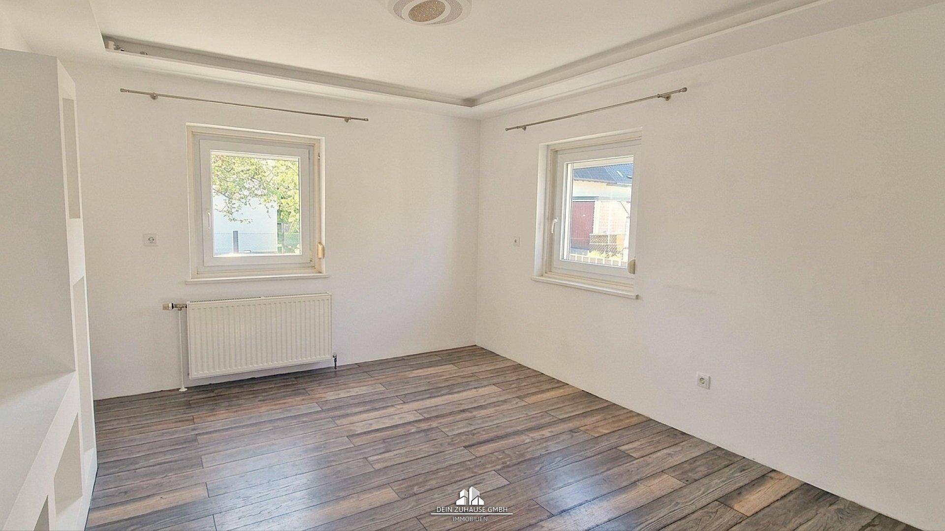 Geräumiger, heller Raum mit modernem Laminatboden und zwei Fenstern, bereit zur individuellen Gestaltung.