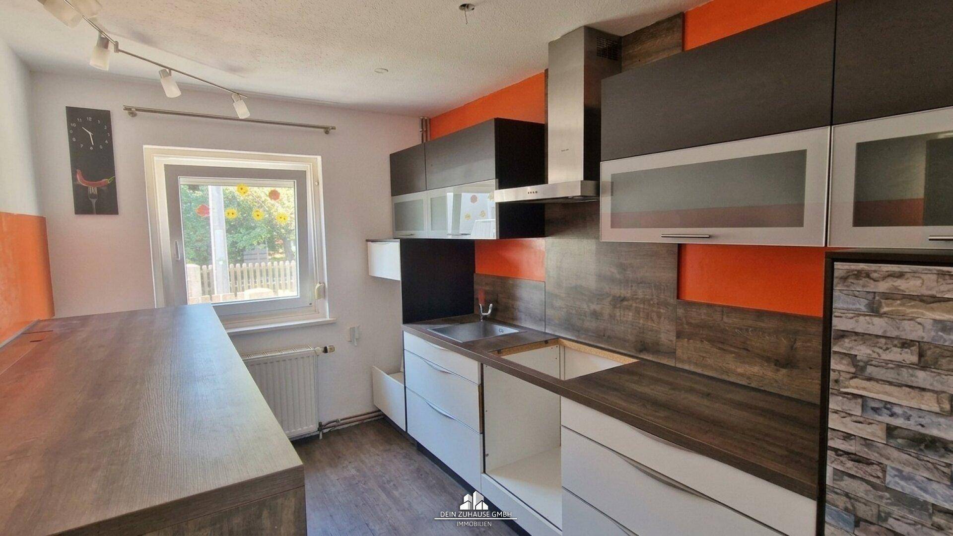 Moderne Küche mit orangefarbenen Akzentwänden, dunklen Arbeitsplatten und integrierter Dunstabzugshaube.