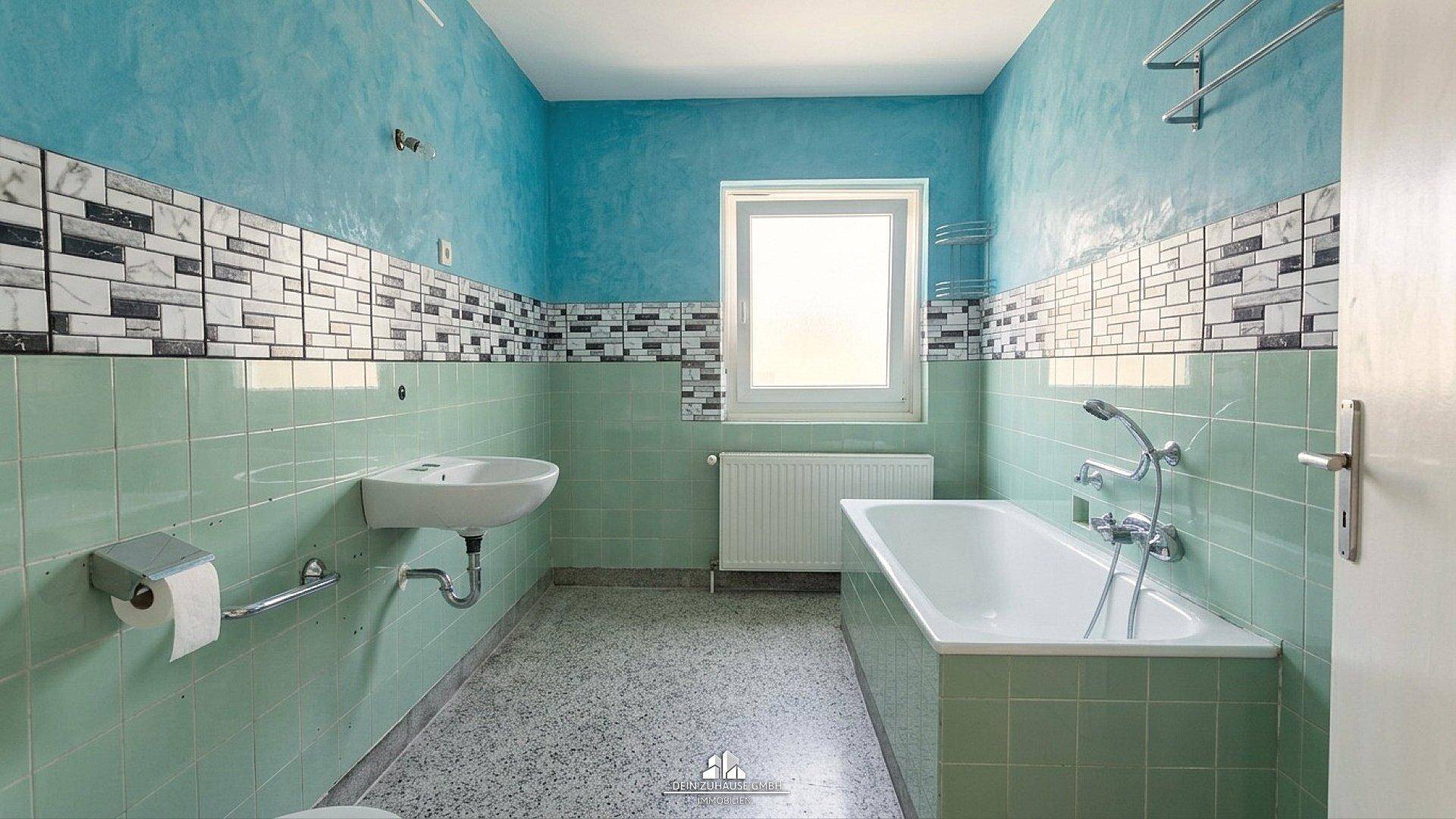 Badezimmer im 80er-Jahre-Stil mit blauen Wänden, grünen Fliesen, Badewanne und Waschbecken.