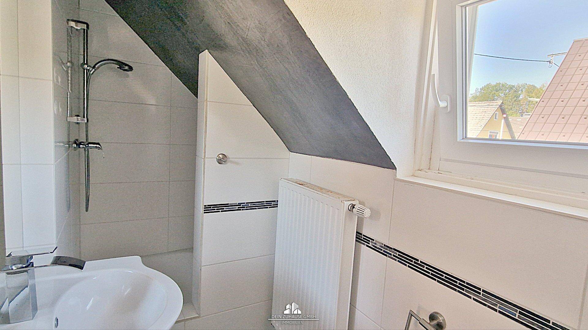 Modernes Badezimmer im Dachgeschoss mit Dusche, Waschbecken und schrägen Wänden.