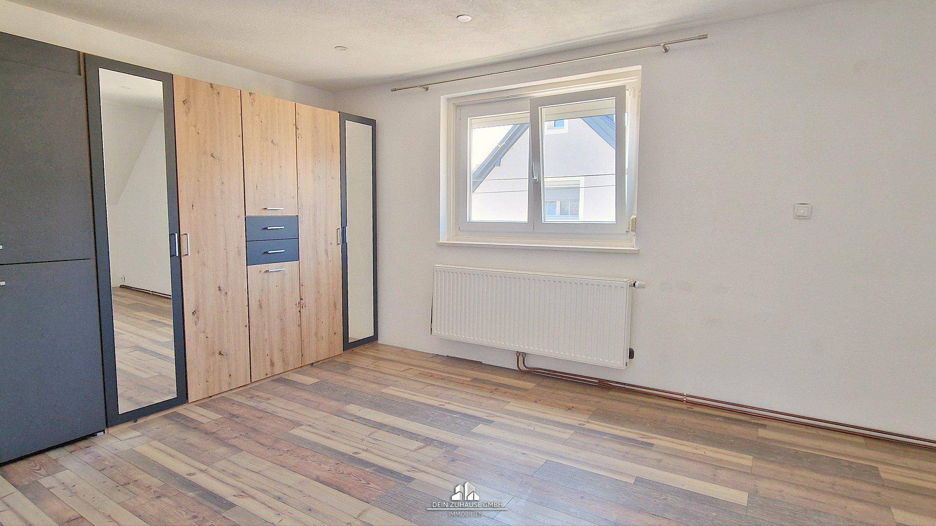 Schlafzimmer mit Laminatboden, großem Fenster und einem modernen Kleiderschrank mit Spiegeltüren.
