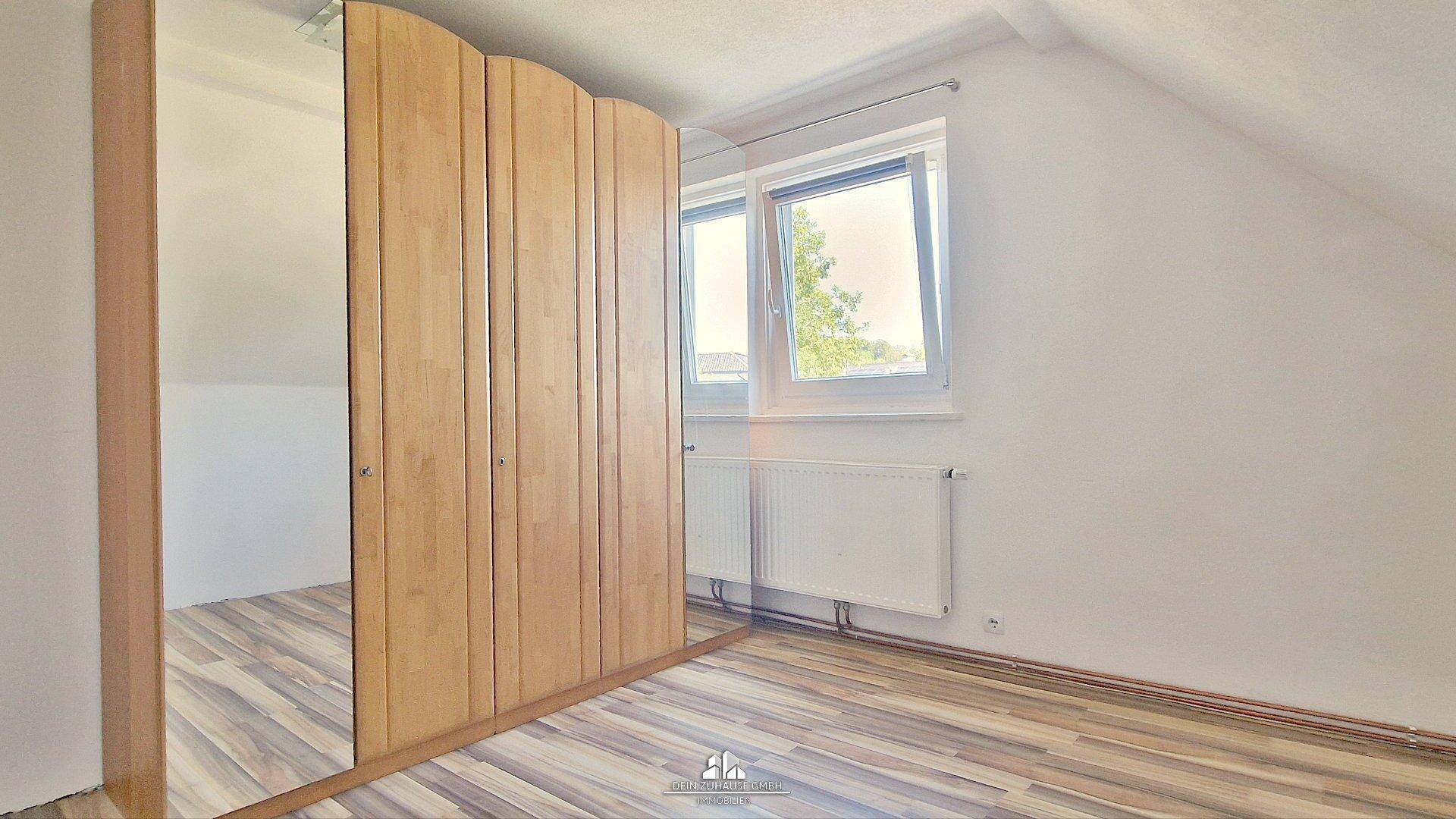 Schlafzimmer im Dachgeschoss mit Laminatboden, Fenster und einem großen Spiegelschrank.