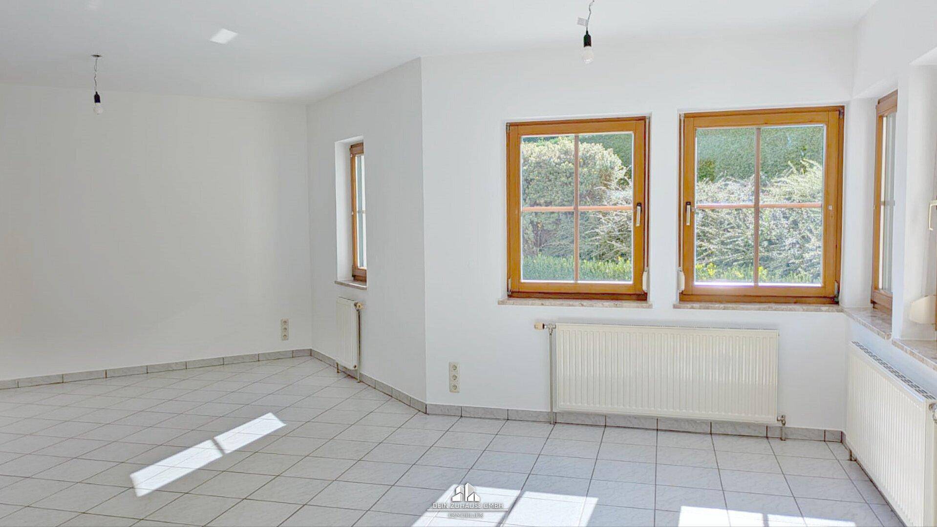 Heller, leerer Raum mit Fliesenboden, weißen Wänden und mehreren Holzfenstern.