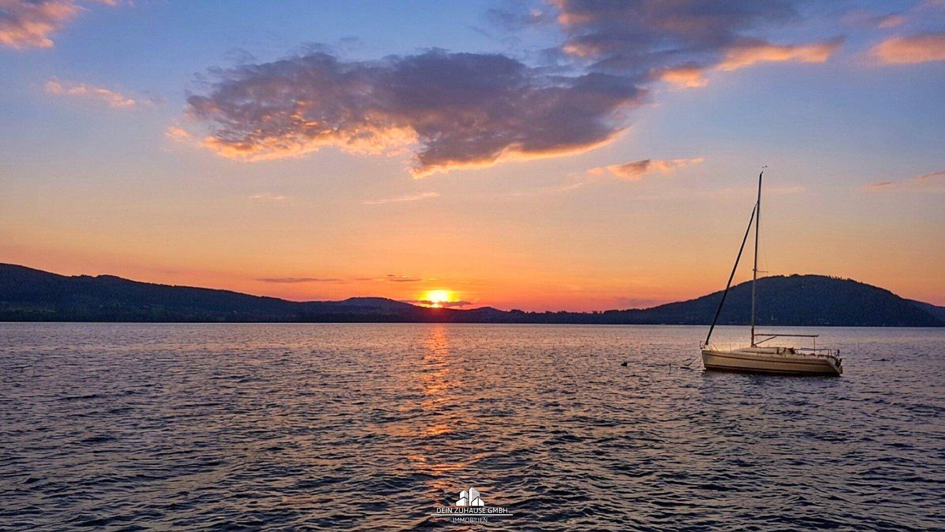 Romantischer Sonnenuntergang über dem See mit einem Segelboot im Vordergrund.