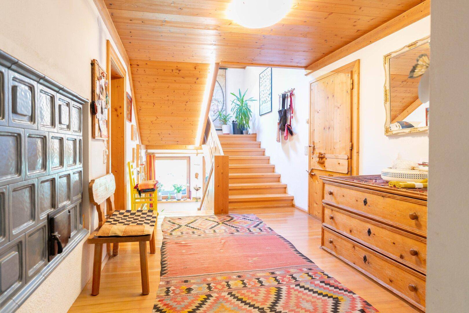 Gemütlicher Flur mit Holzvertäfelung, Treppe und einem traditionellen Kachelofen.