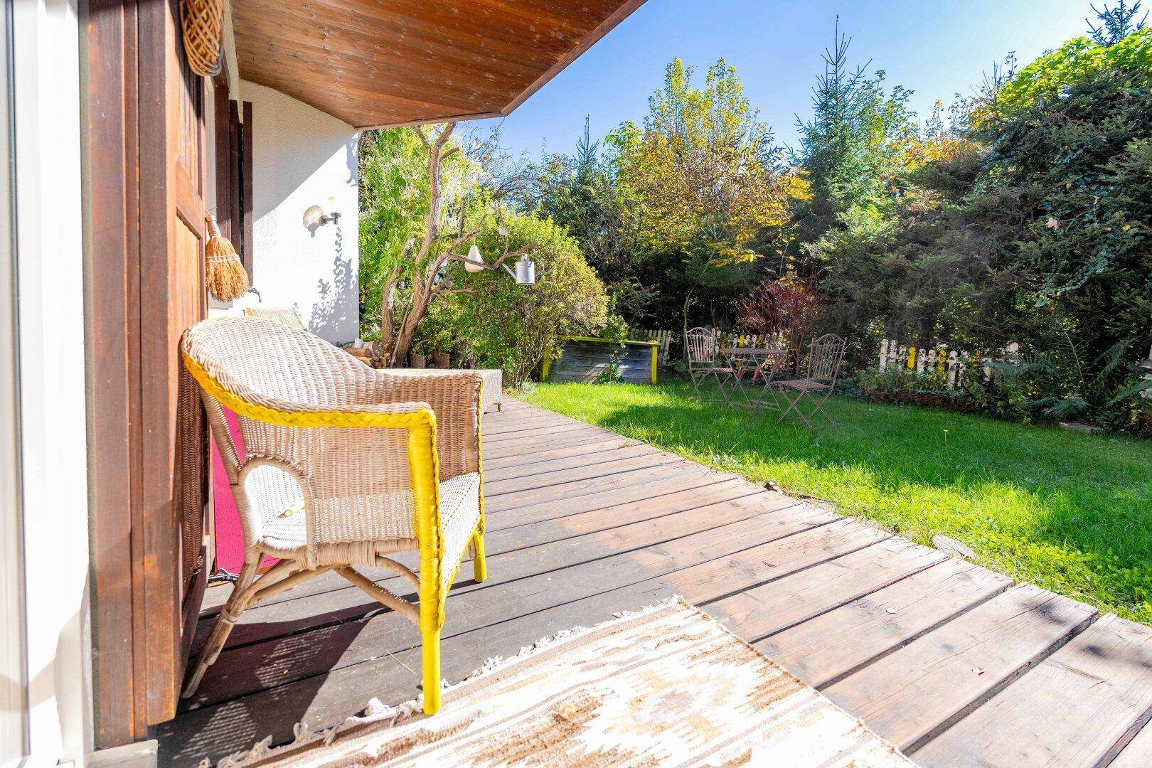 Sonniger Terrassenbereich mit Holzdeck und Blick auf den grünen Garten.