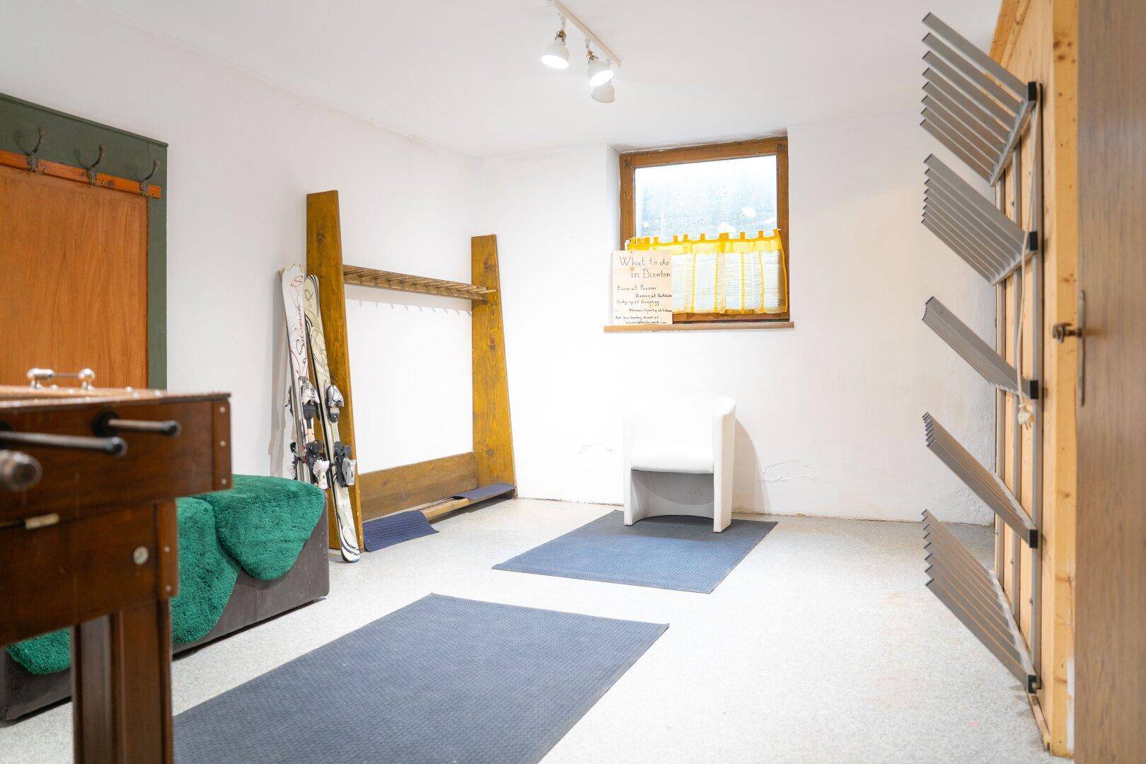 Funktionaler Skiraum im Untergeschoss mit Skihaltern, Ablagemöglichkeiten und einem Fenster.