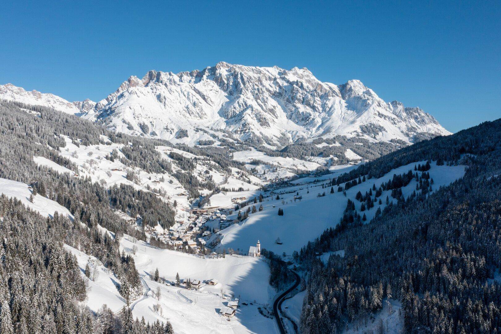 Winterliche Alpenlandschaft mit schneebedeckten Bergen, Wäldern und einem idyllischen Dorf.