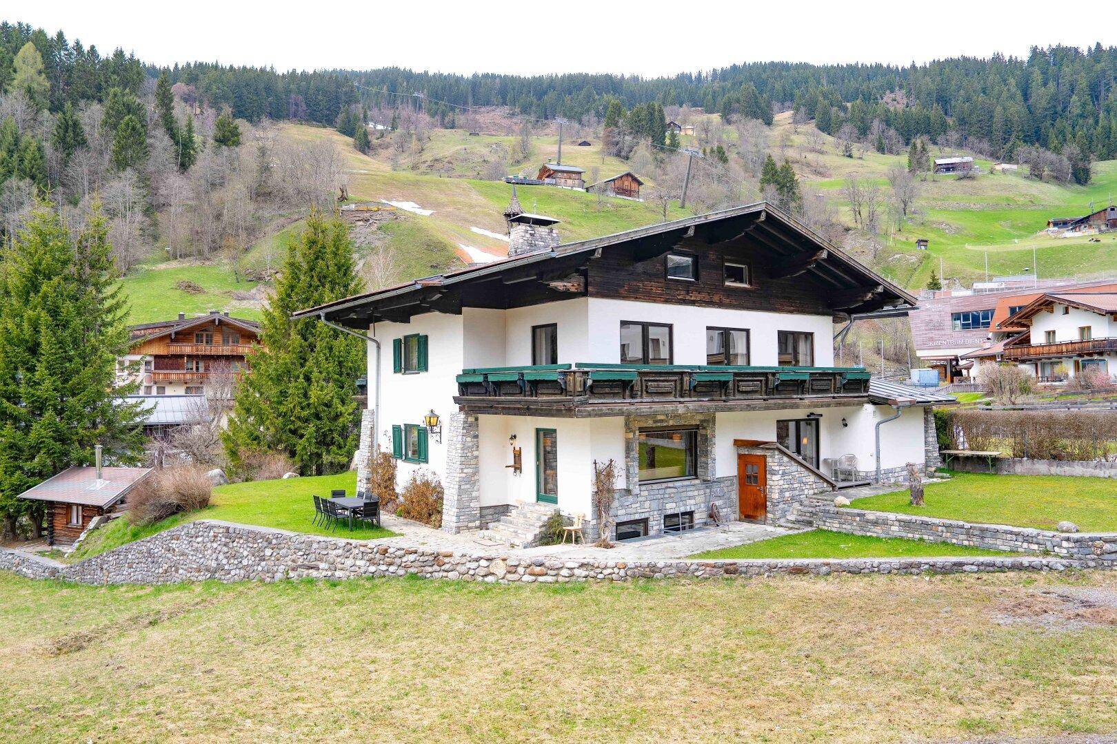 Traditionelles alpines Haus mit Balkonen, Steinfassade und umgebender grüner Natur.